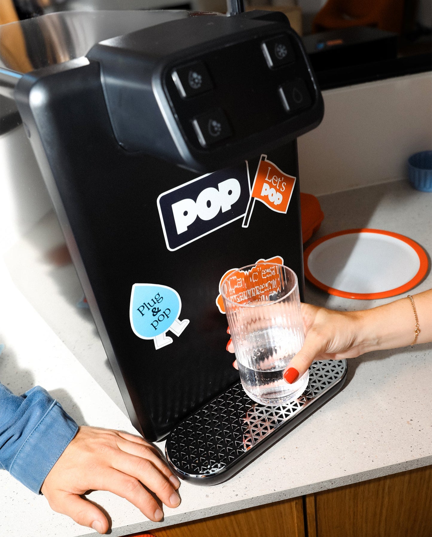 Gros plan sur une main remplissant un verre d’eau avec une fontaine POP décorée de stickers colorés.