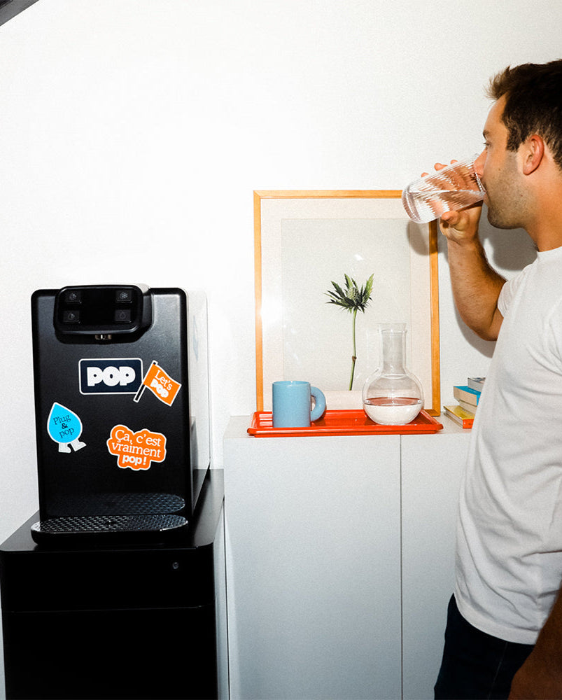 Un homme boit de l’eau depuis une fontaine POP dans un bureau moderne – version mobile.	
